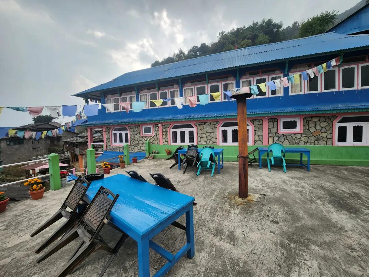 Blue teahouse guesthouse in Ulleri, Nepal with colourful prayer flags and outdoor seating area on the mountain terrace