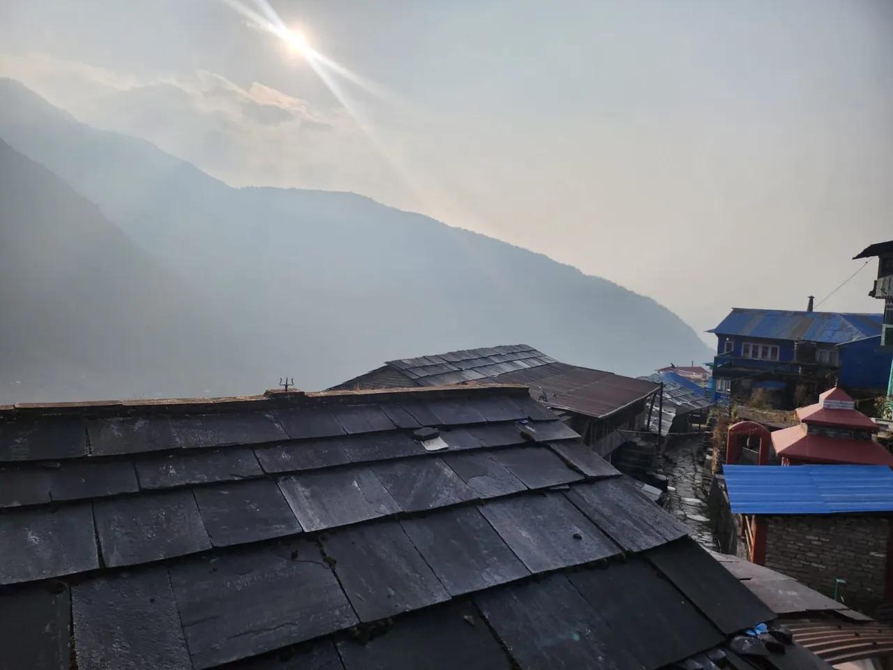 Traditional stone slate rooftops of Ulleri village with misty mountains and morning sunlight in background, Annapurna foothills Nepal